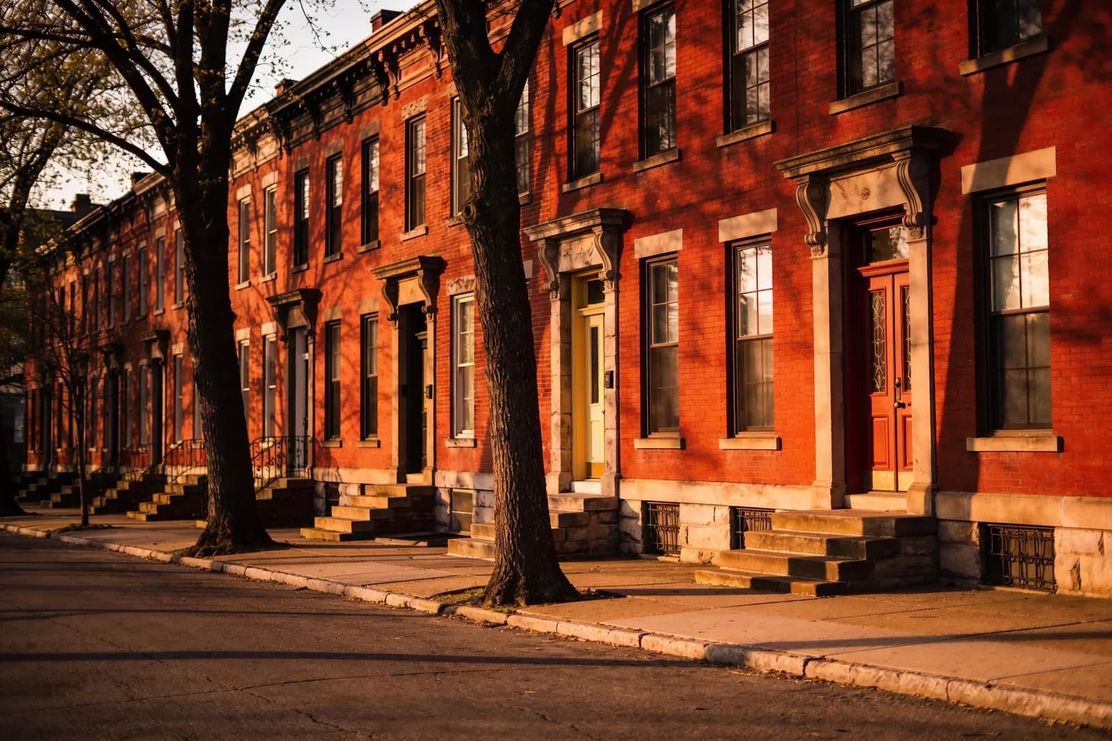 A row of nineteenth-century red brick townhouses on a quiet street in late golden light.